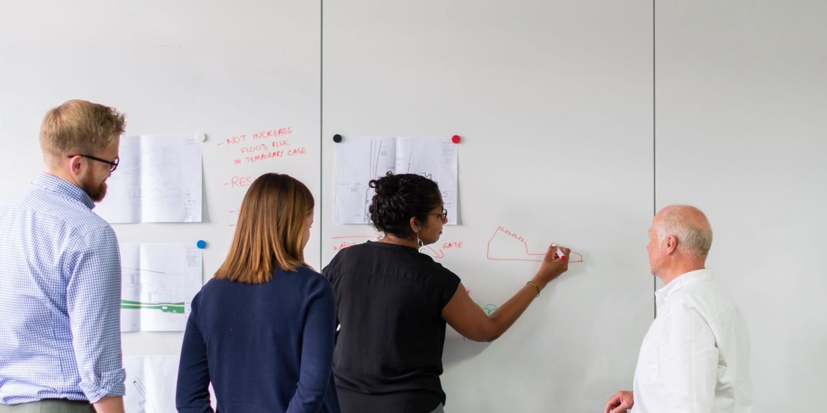A team collaborates around a whiteboard, designing complex AI systems that move beyond simple prompts to integrate memory and real-time data.